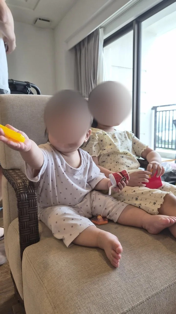 거실 의자에 앉아 장난감을 들고 있는 두 아이